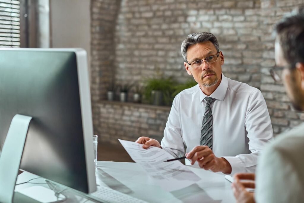 Mężczyzna wyjaśniający zawiłości dokumentów drugiemu mężczyźnie w gabinecie
